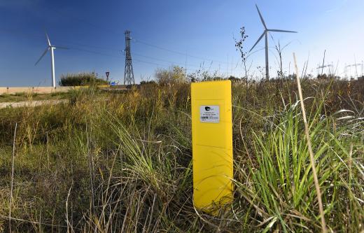 Borne jaune indiquant la présence d’une canalisation de transport de gaz naturel haute pression, à proximité d’une ligne de haute tension et d’une éolienne.
