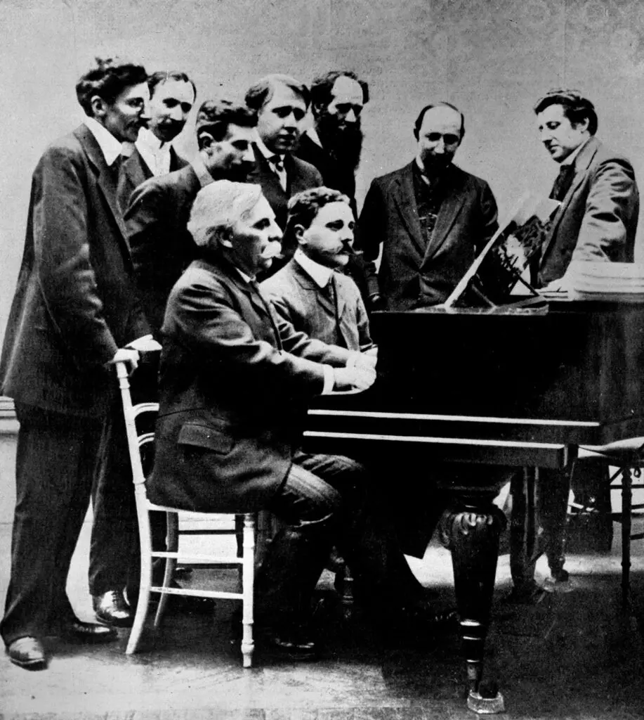 Gabriel Fauré (1845-1924) et Jean Roger-Ducasse (1873-1954), au piano, accompagnés, derrière eux, de gauche à droite, de Louis Aubert, A.Z. Mathot, Maurice Ravel, André Caplet, Charles Kœchlin, Émile Vuillermoz et Jean Huré. © Albert Harlingue / Roger-Viollet.